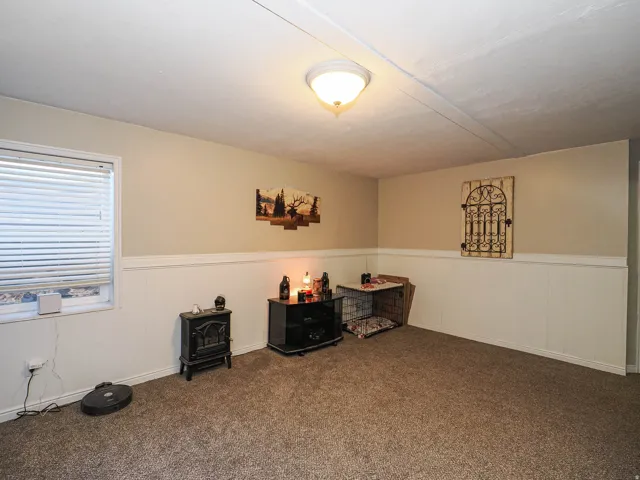 Carpeted interior space featuring a window with horizontal blinds, neutral-toned walls, white wainscoting, and a ceiling-mounted light fixture