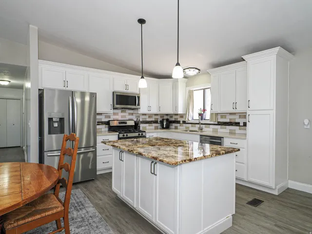 Modern kitchen featuring a central island with a polished stone countertop, white cabinetry with dark hardware, stainless steel appliances, a mosaic tile backsplash, and wood-finish flooring