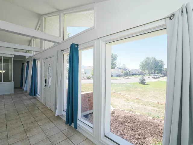 Front entry sunroom featuring an abundance of natural light, vaulted ceiling with exposed beams, tiled flooring, and a decorative front door with side windows