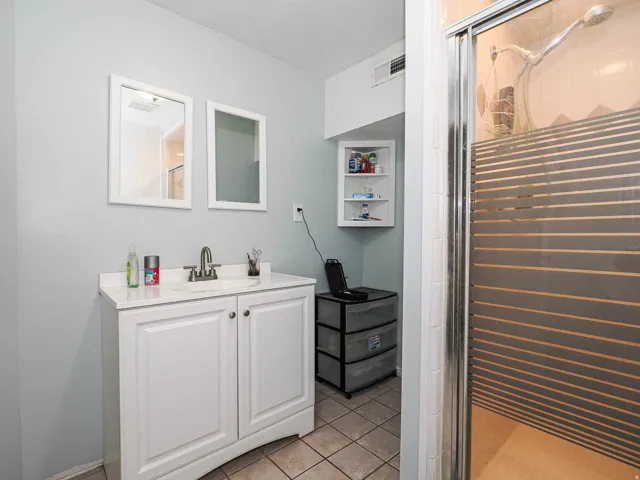 Bathroom featuring a white vanity with an integrated sink, dual wall-mounted mirrors, and a glass-enclosed shower with a striped privacy panel