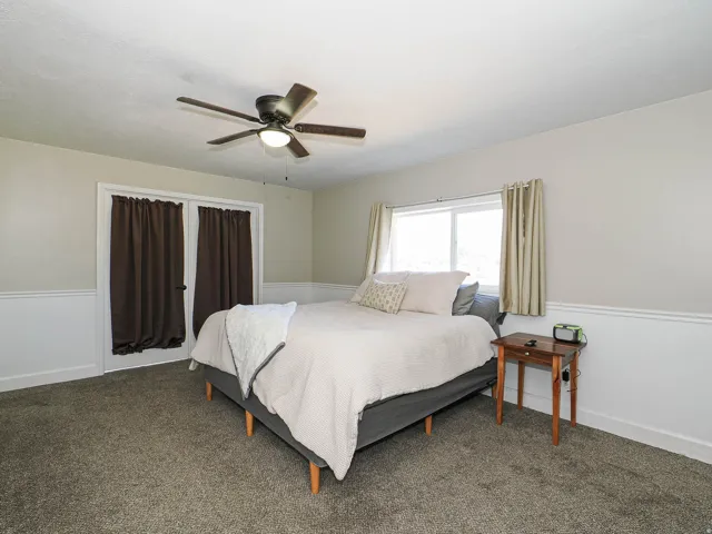 Carpeted room featuring a ceiling fan with integrated lighting, dual white French doors, a single window, and wainscoting