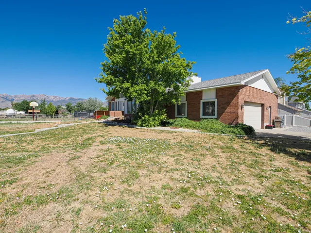 Brick exterior home featuring a two-car garage, mature tree, and mountain backdrop