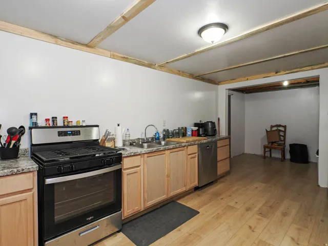 Open kitchen space featuring light wood-finish flooring, stainless steel appliances, a double basin sink, and granite-style countertops