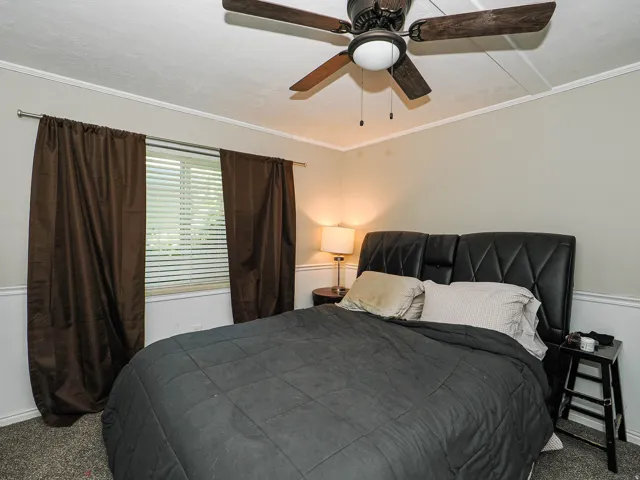 Room featuring a ceiling fan with integrated lighting, crown molding, and wainscoting