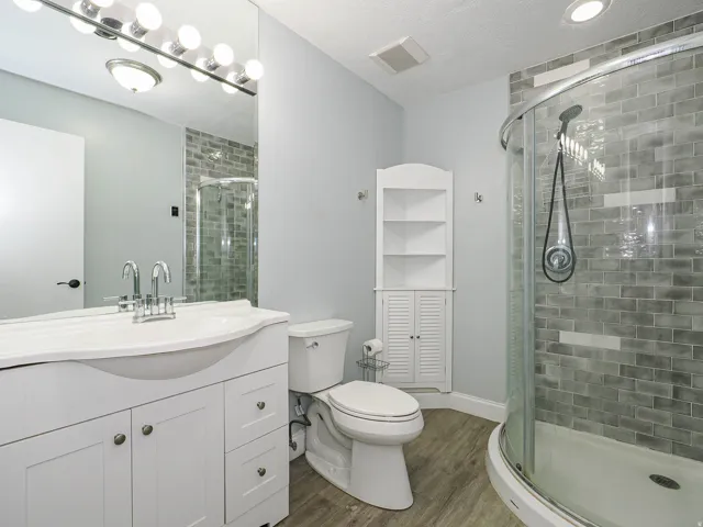 Bathroom featuring a curved glass shower enclosure with subway tile surround, a single vanity with an integrated sink, a large wall-mounted mirror, and wood-finish flooring