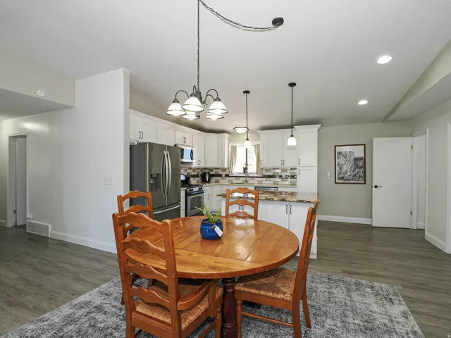 Kitchen and dining area featuring white cabinetry, stainless steel appliances, pendant lighting, and wood-finish flooring