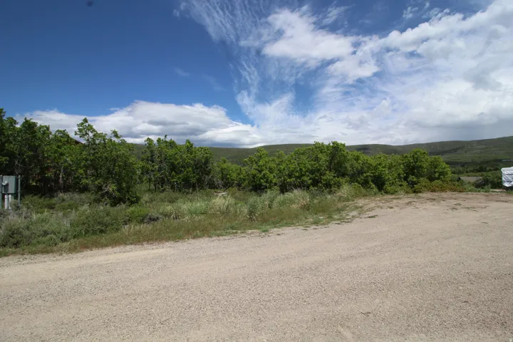 Expansive undeveloped lot featuring a gravel surface, natural vegetation, and distant rolling hills