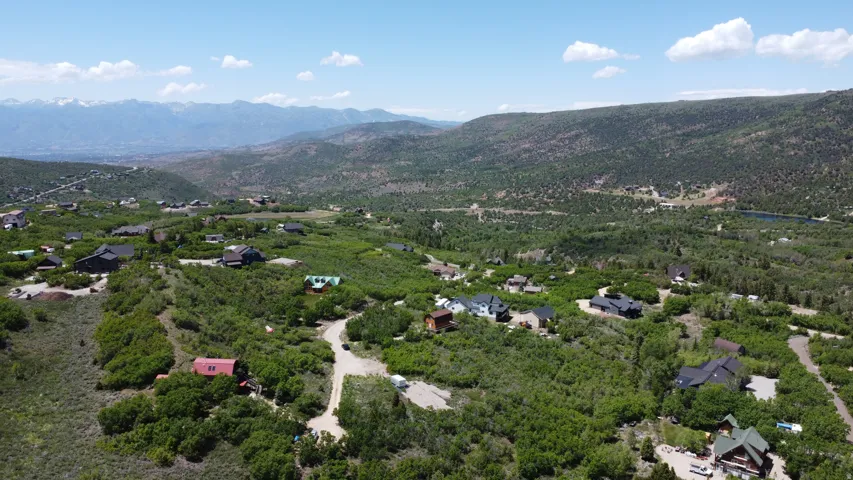 Expansive mountain landscape featuring numerous properties nestled within abundant greenery and distant snow-capped peaks