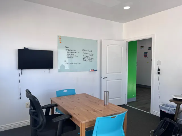 Recessed lighting illuminates this versatile space featuring a white wall-mounted television, a glass whiteboard, and a white interior door with a paneled design