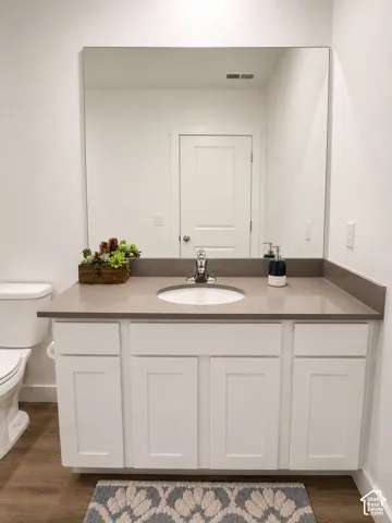 White shaker-style vanity with an integrated sink and light gray countertop, complemented by wood-finish flooring and a frameless wall mirror