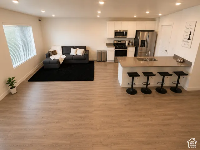 Open-concept living space featuring wood-finish flooring throughout, recessed lighting, and a modern kitchen with white cabinetry, stainless steel appliances, and a peninsula with seating