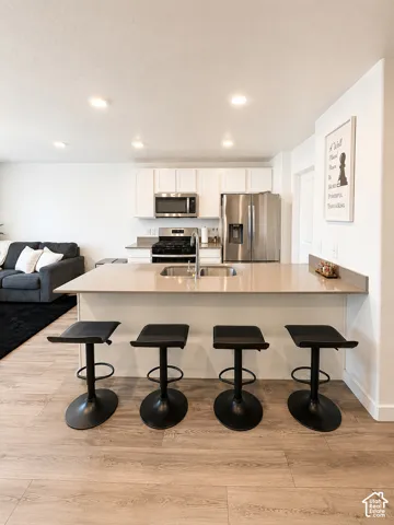 Open-concept kitchen featuring recessed lighting, stainless steel appliances, white cabinetry, a double basin sink, and a peninsula with seating