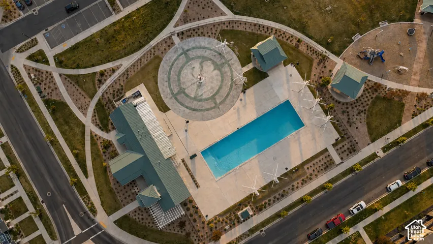 Community recreation center featuring a swimming pool, clubhouse with a green roof, circular paved plaza, and pathways surrounded by landscaping