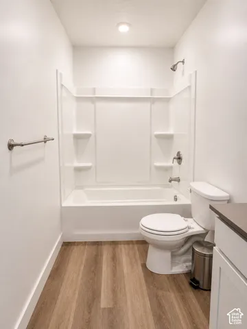 Bathroom featuring a white tub and shower combination with chrome fixtures, a white toilet, and wood-finish flooring