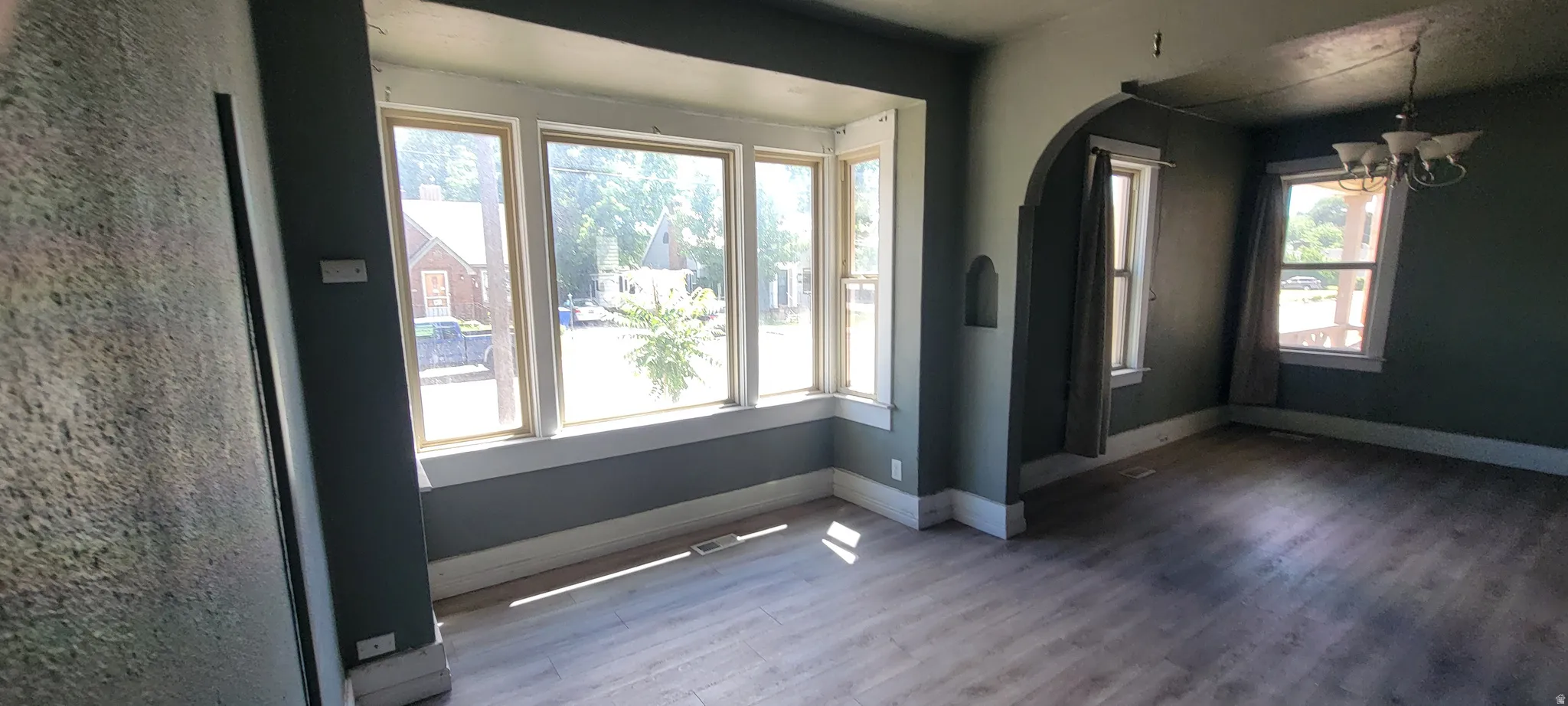 Bay window with white trim, wood-finish flooring, recessed wall niche, and an arched doorway