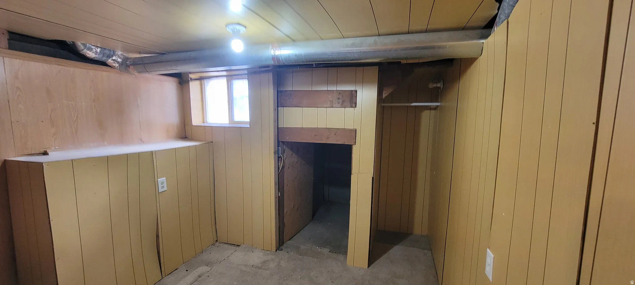 Utility space featuring wood paneling, exposed ductwork, a single window, built-in shelving, and a recessed entryway