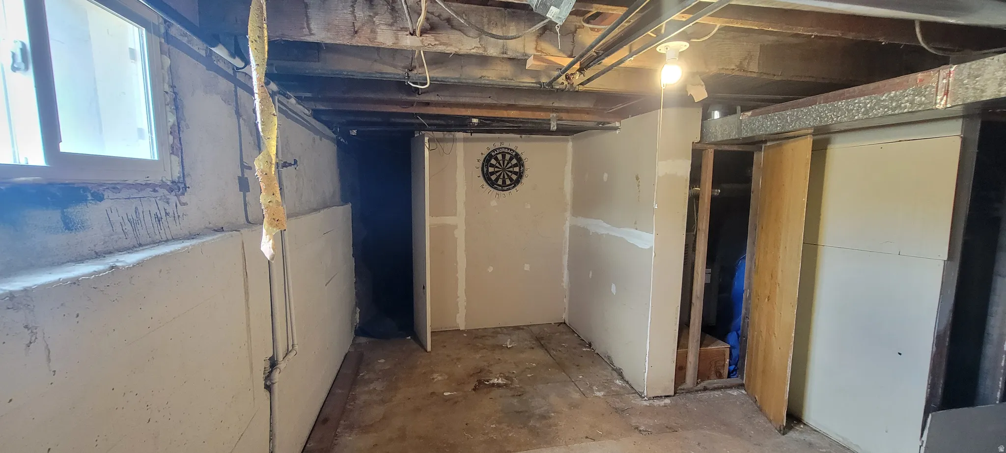 Unfinished basement area featuring exposed ceiling joists, concrete foundation walls, and a visible window with a white frame