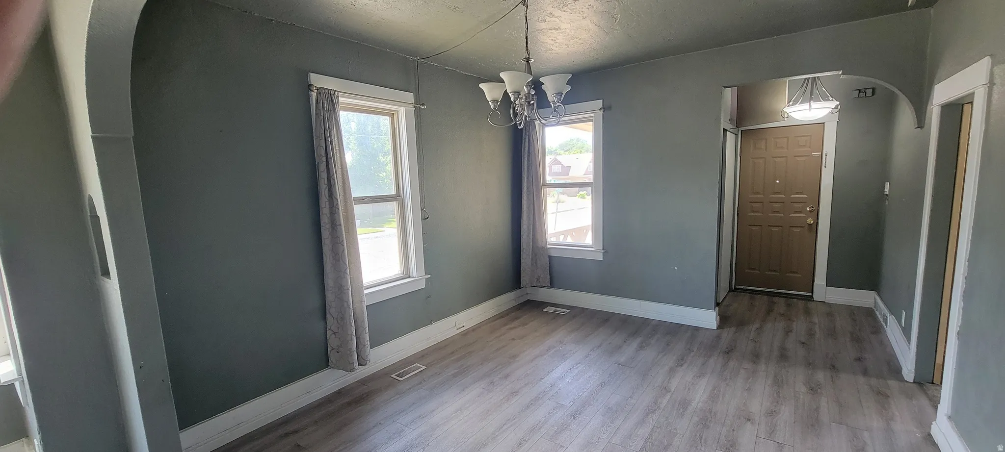 Open concept living space featuring wood-finish flooring, multiple windows, a decorative chandelier, and an arched entryway