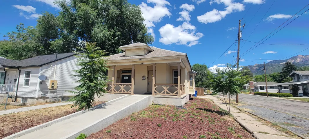 Single-story residence featuring a covered front porch with decorative wood railings, a neutral-toned exterior, and a gabled roofline