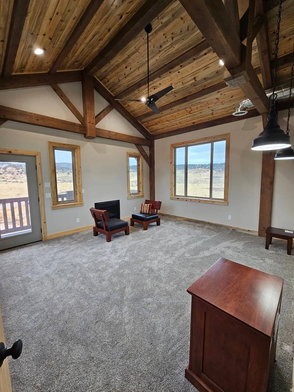 Spacious master bedroom featuring a vaulted wood-plank ceiling, exposed wood beams, and a large picture window with fireplace