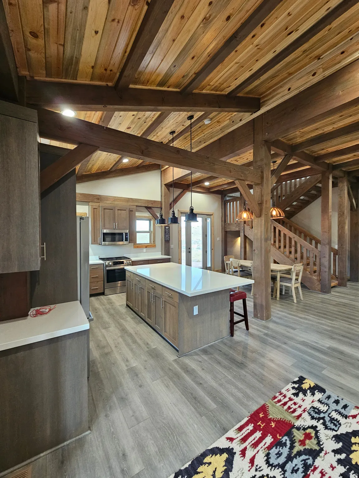 Open-concept kitchen and dining area featuring wood-finish flooring, exposed wood beams, wood panel ceilings, a kitchen island with a light-toned countertop, and stainless steel appliances