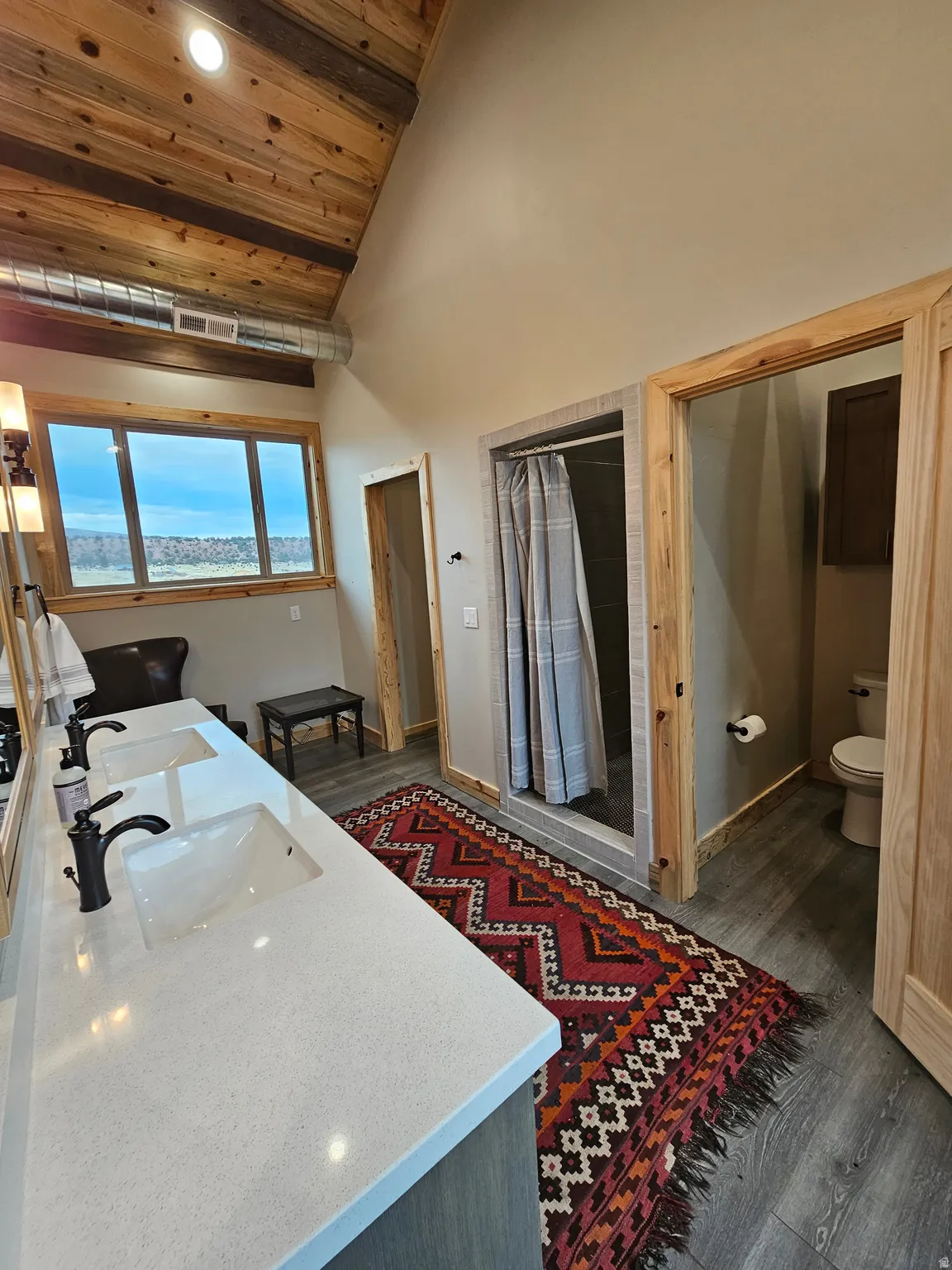 Double vanity with a light-toned countertop and matte black fixtures, exposed wood plank vaulted ceiling, and a tiled shower