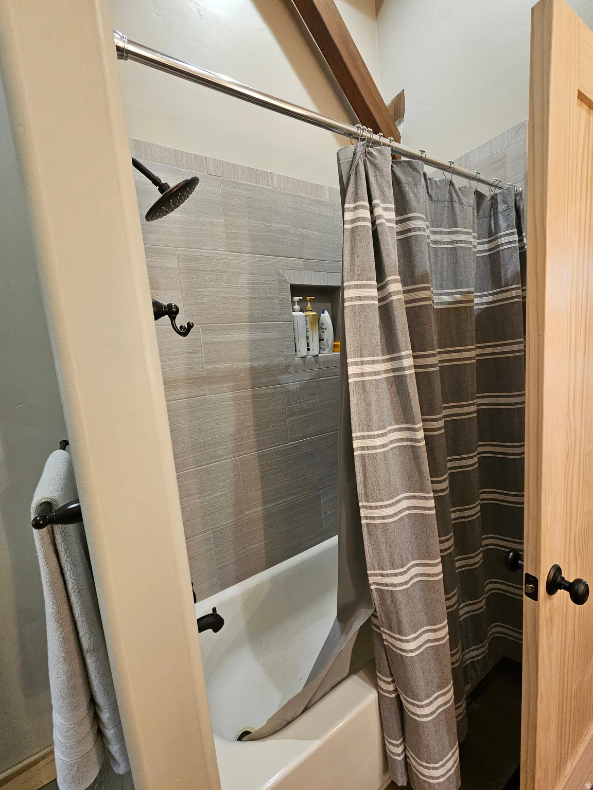 Bathtub and shower combination featuring horizontal gray tile surround, recessed shower niche