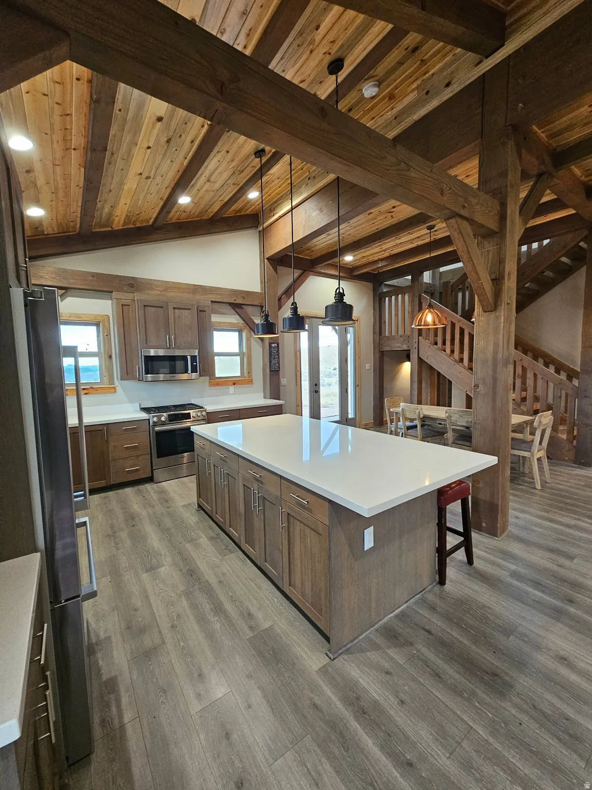 Spacious kitchen featuring a large central island with white countertop, wood-finish cabinetry, stainless steel appliances, and wood-finish flooring