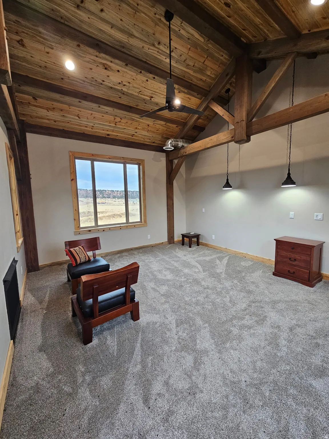 Spacious master bedroom featuring a vaulted wood-plank ceiling, exposed wood beams, and a large picture window with fireplace