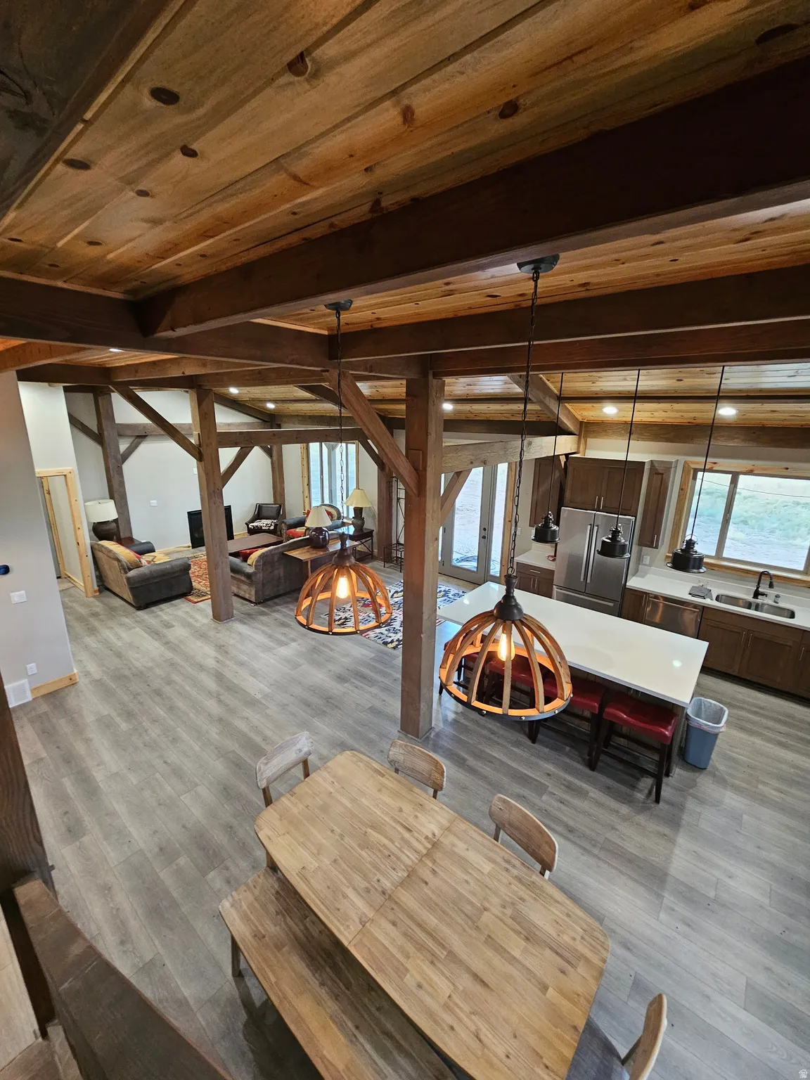 Open-concept kitchen and dining area featuring wood-finish flooring, exposed wood beams, wood panel ceilings, a kitchen island with a light-toned countertop, and stainless steel appliances