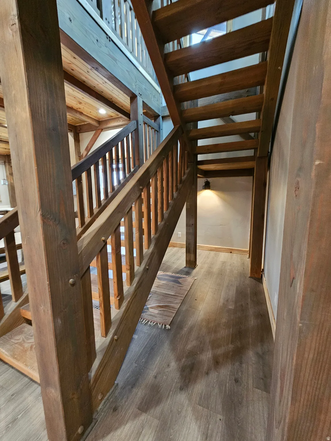 Wood-finish flooring throughout, complemented by a multi-level wooden staircase with exposed beams and a wooden railing