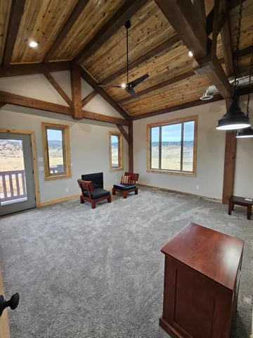 Spacious master bedroom featuring a vaulted wood-plank ceiling, exposed wood beams, and a large picture window with fireplace