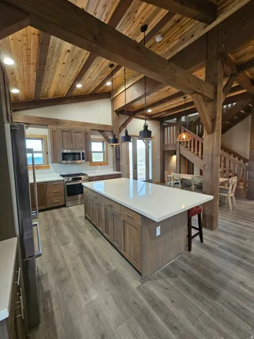 Spacious kitchen featuring a large central island with white countertop, wood-finish cabinetry, stainless steel appliances, and wood-finish flooring