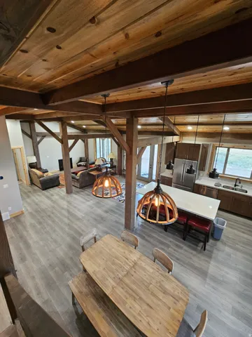 Open-concept kitchen and dining area featuring wood-finish flooring, exposed wood beams, wood panel ceilings, a kitchen island with a light-toned countertop, and stainless steel appliances