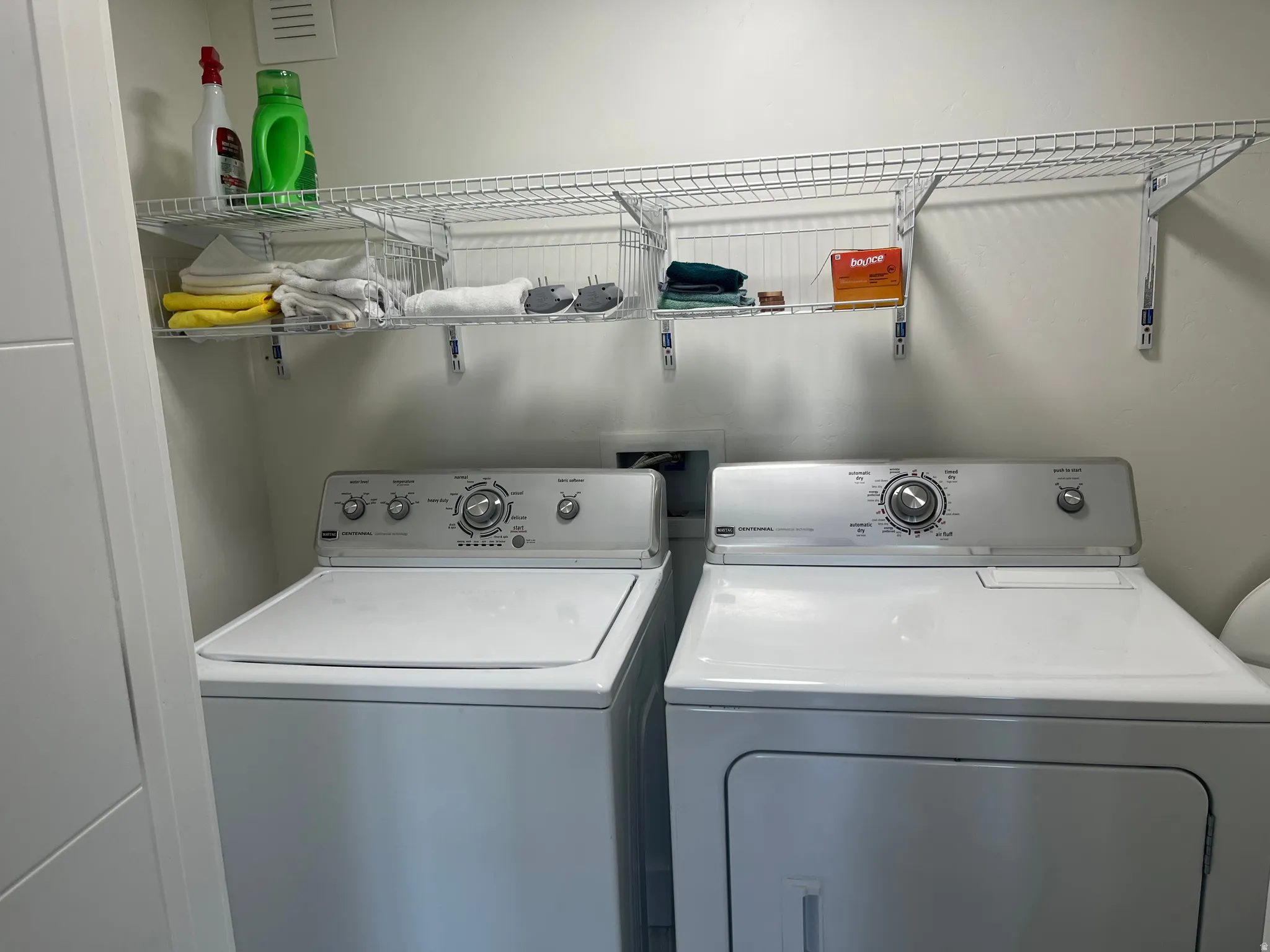 Dedicated laundry area featuring a top-load washer, a front-load dryer, and a wall-mounted wire shelving system