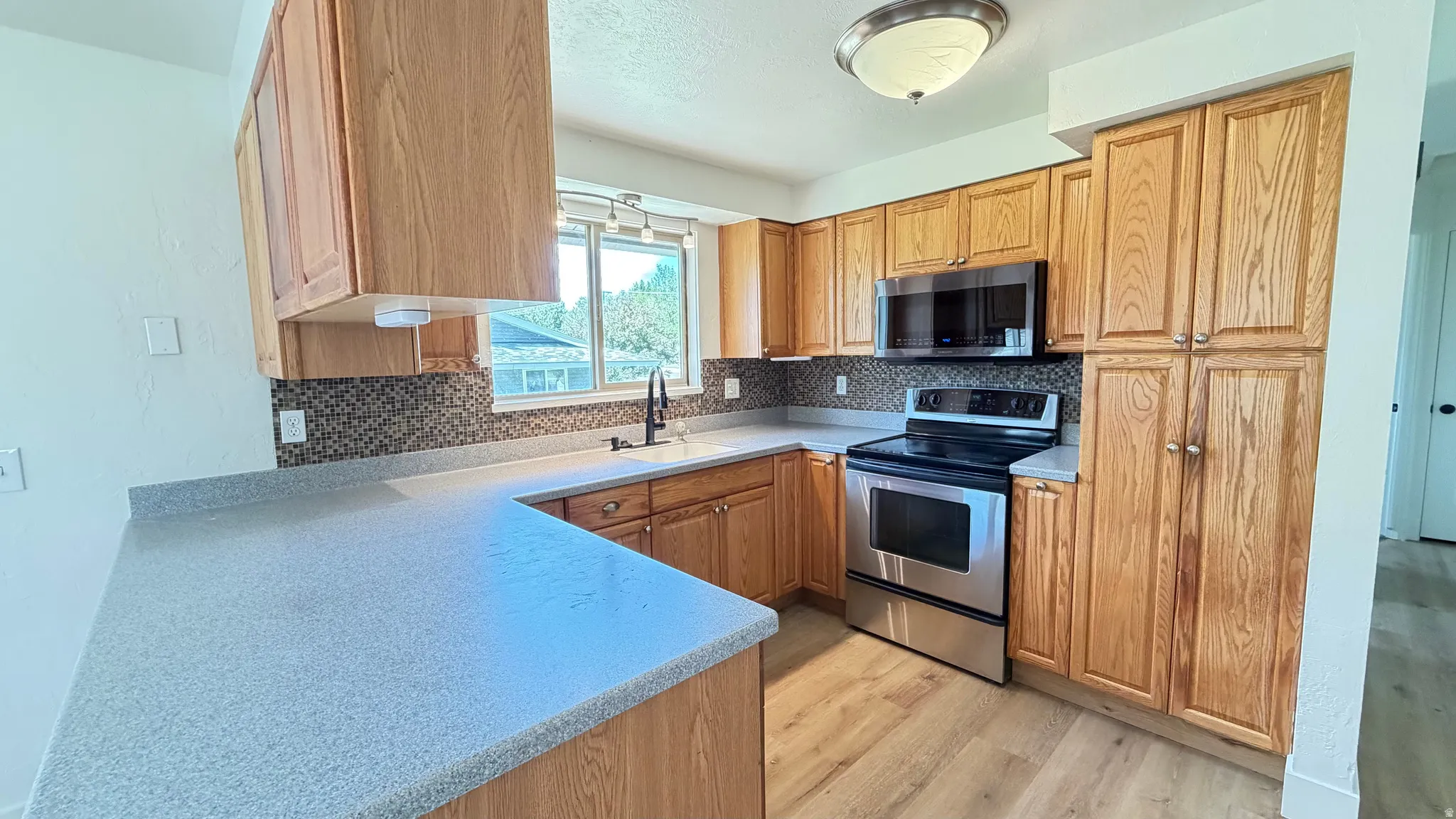 Kitchen featuring wood cabinetry, light-toned countertops, a mosaic tile backsplash, stainless steel appliances, and wood-finish flooring
