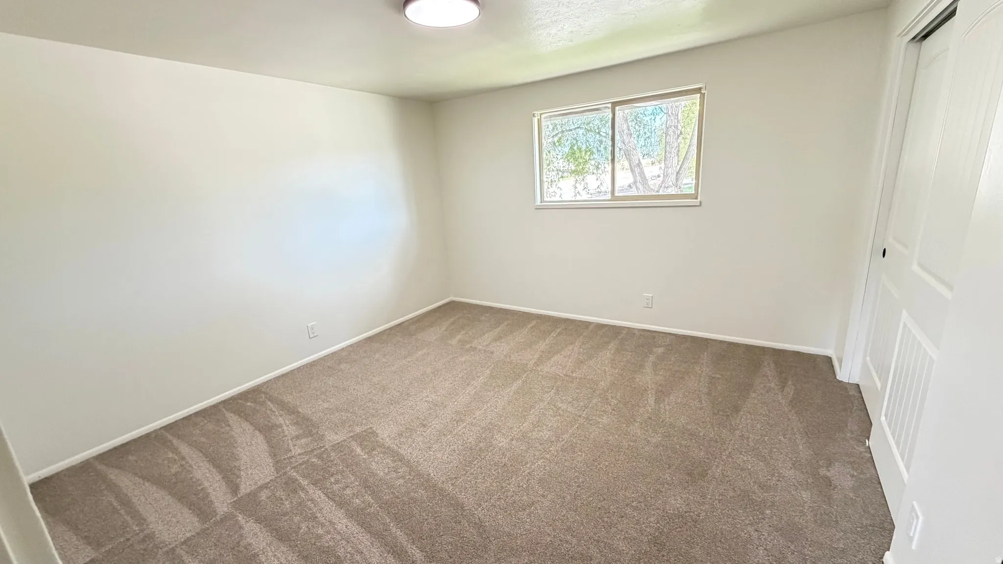 Neutral tone wall paint, carpet flooring, a window, baseboard trim, and a flush mount ceiling light fixture