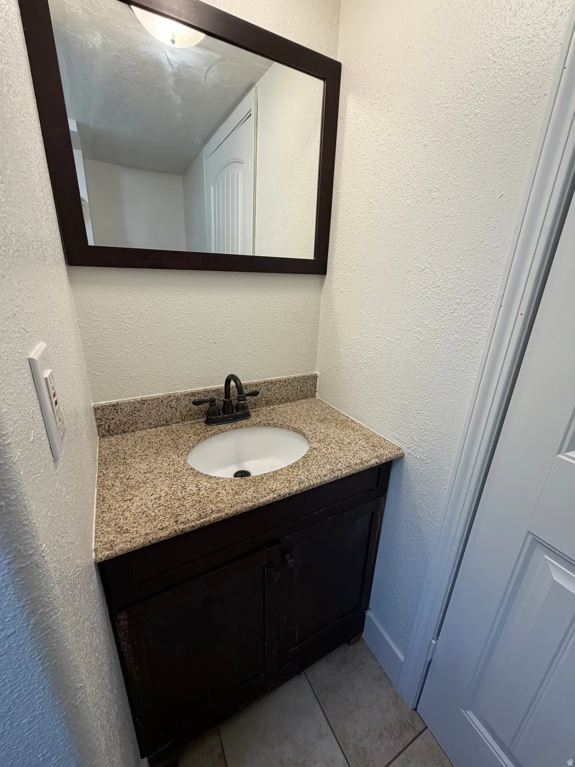 Vanity with a granite-style countertop, undermount sink, and dark wood-finish cabinet