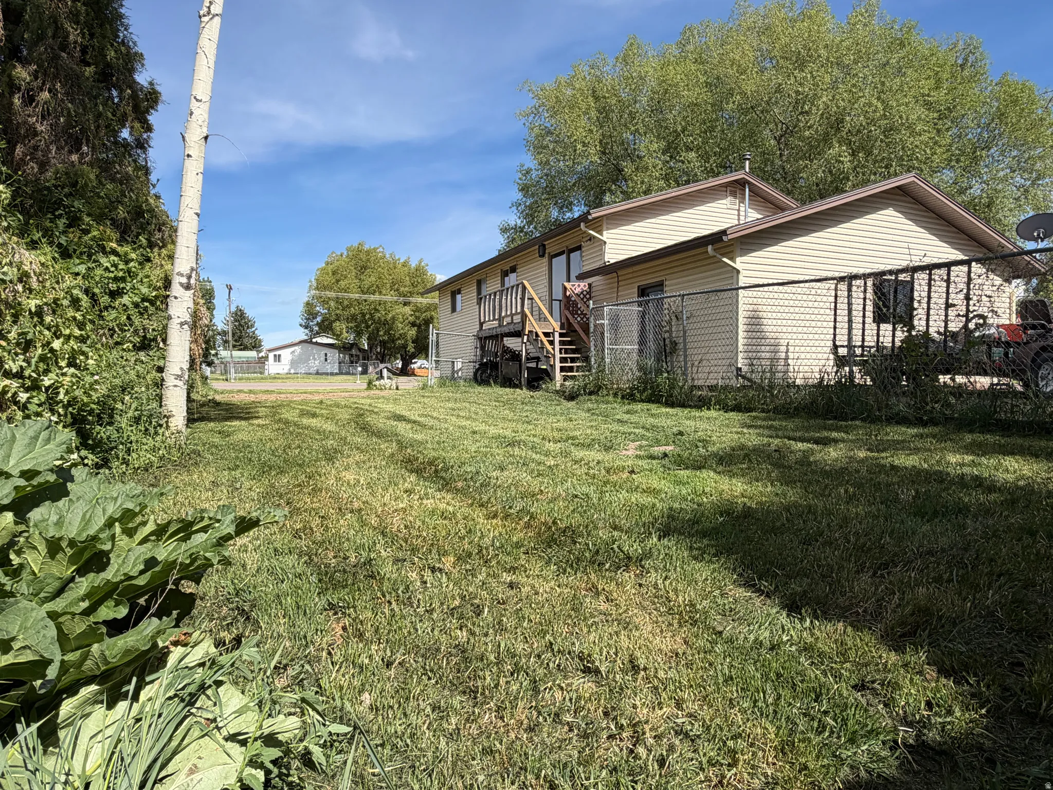 Exterior property with light-colored siding, a multi-level rear deck, a chain-link fence, and a spacious grassy area