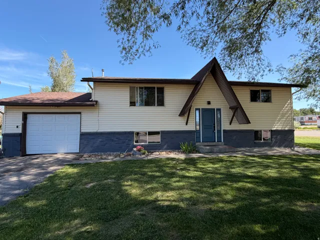 Split-level residence featuring a prominent A-frame entry, two-tone siding, an attached garage with a white panel door, a shingled roof, and a mature tree providing shade