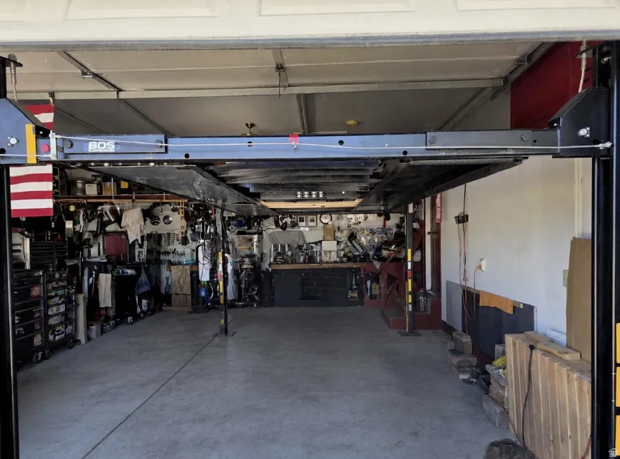 Spacious garage featuring a four-post car lift, concrete flooring, and ample wall storage