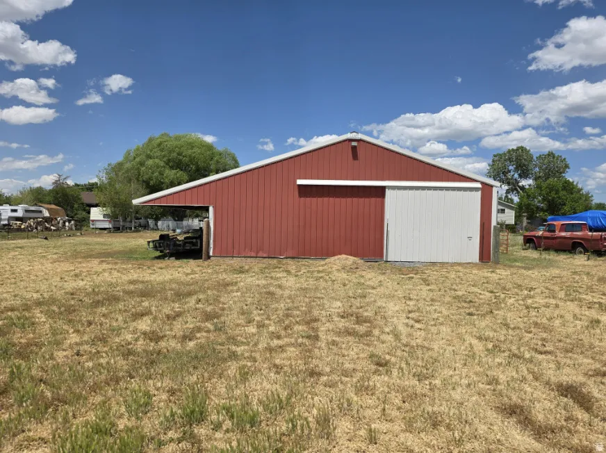 Red metal barn structure featuring a white sliding door, an extended overhang, and a light-colored roofline