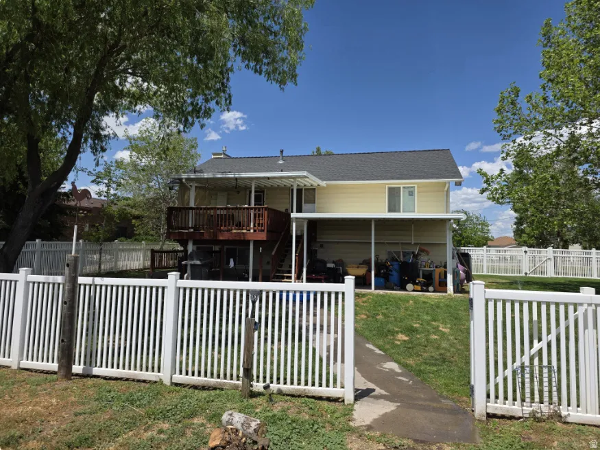 Rear elevation featuring a double-level deck, covered patio, white picket fencing, and mature trees