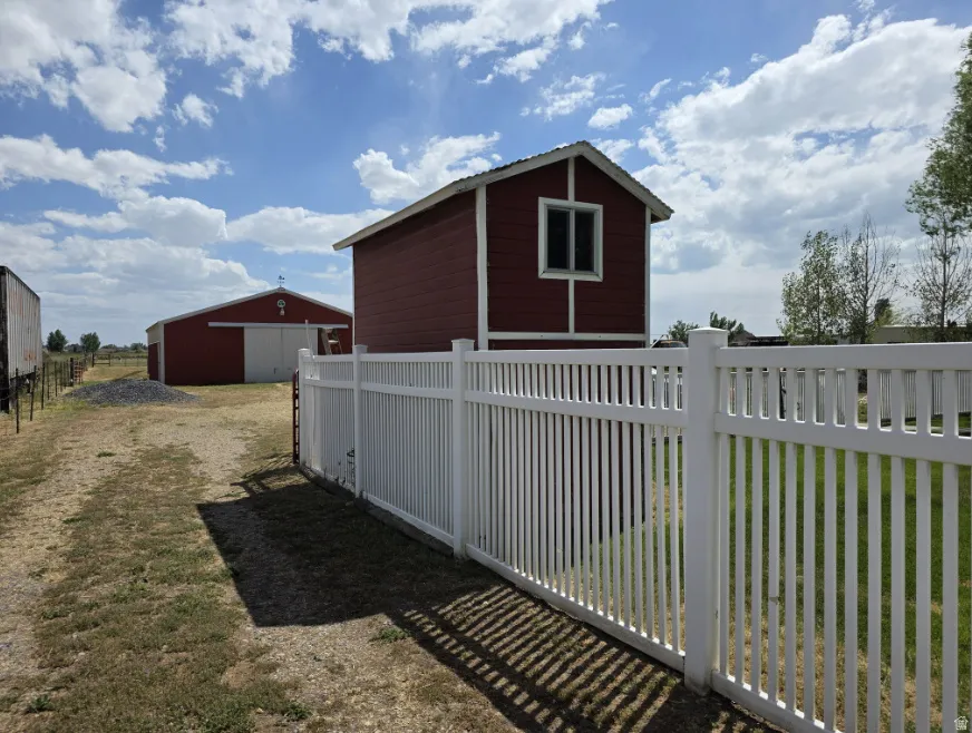 White picket fence enclosing a green space, with a red outbuilding featuring white trim and a single window