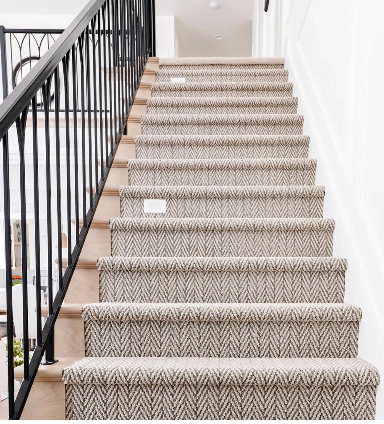 Staircase featuring a patterned runner, hardwood treads, white risers, and black metal balusters with an arched detail