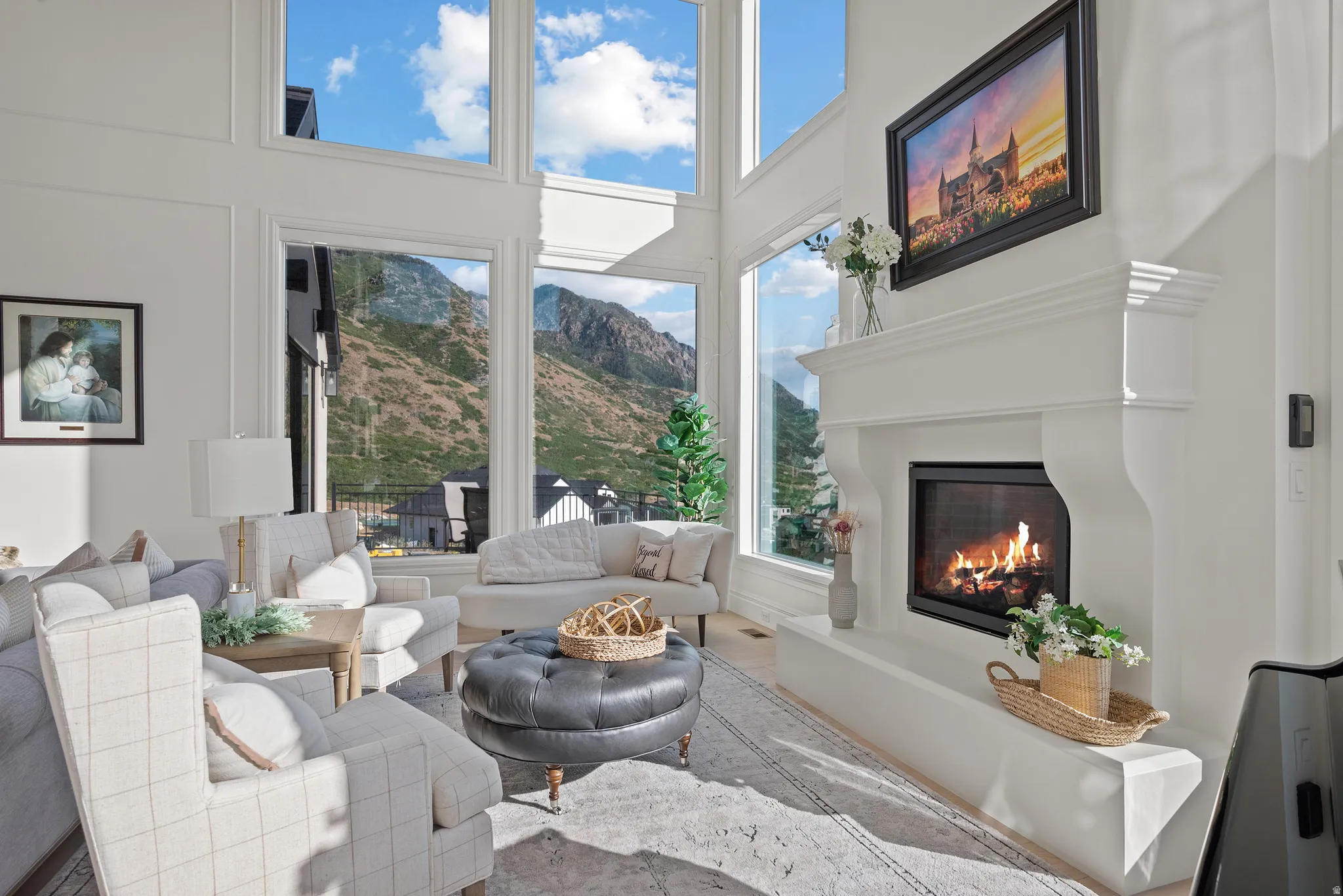 Living room featuring a prominent fireplace with a white mantel and hearth, soaring ceilings, and expansive picture windows
