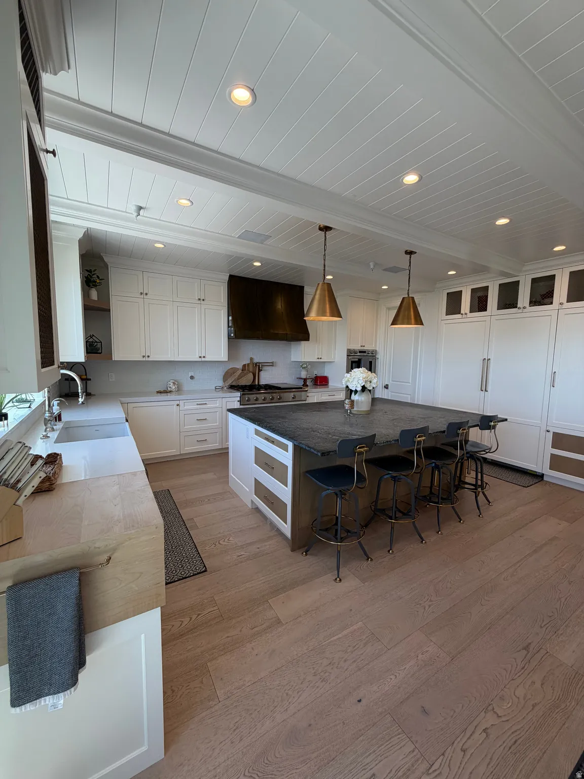 Gourmet kitchen featuring a large central island with seating, extensive white cabinetry, brass pendant lighting, and wood-finish flooring