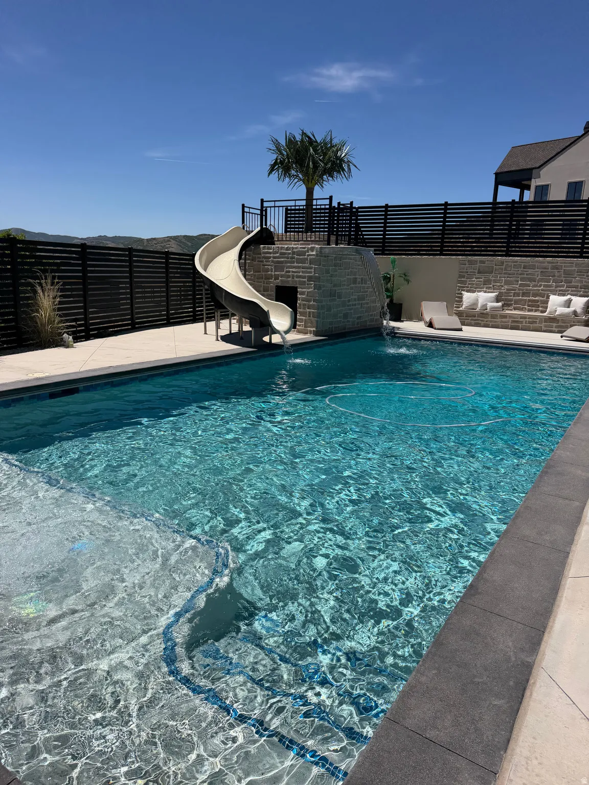Rectangular swimming pool featuring integrated steps and a stone-clad water slide