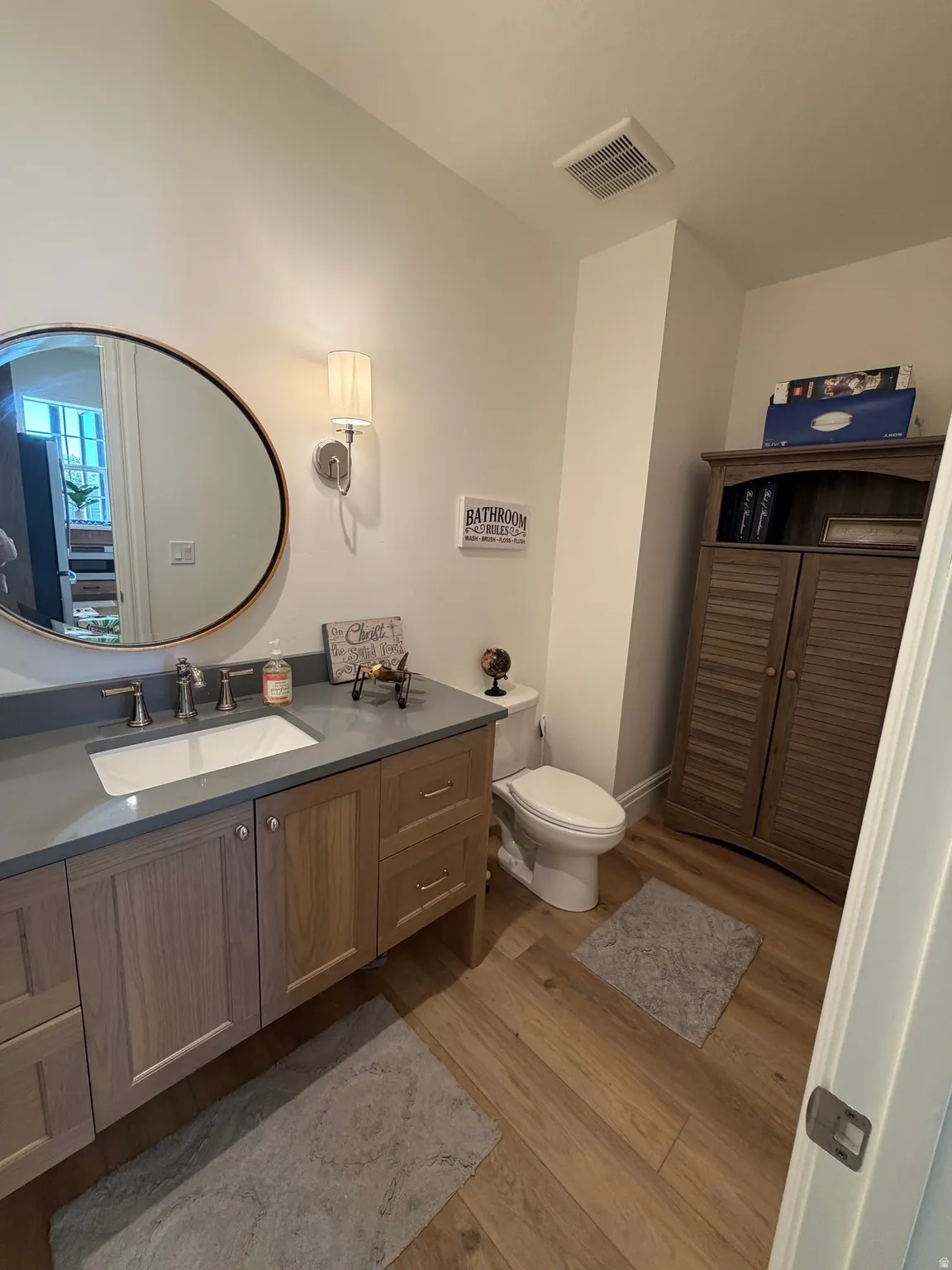 Bathroom featuring a wood-finish vanity with a single basin sink, gray countertop, and bronze hardware