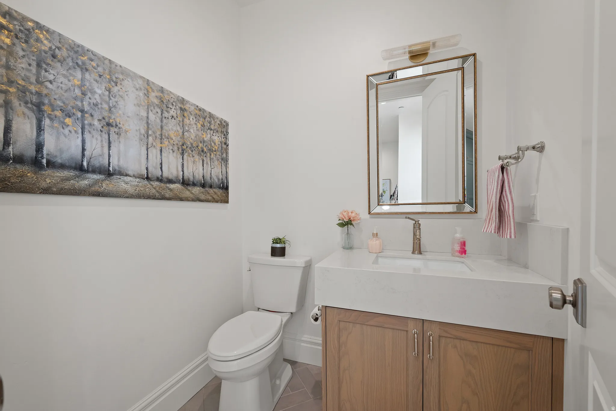Powder room featuring a light wood vanity, white countertop with integrated sink, and an ornate framed mirror with an overhead light fixture